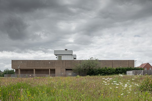 Exterior of the bunker in green field showing grey low imposing building.