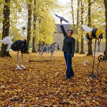 Photo of artist Michelle stood in a wooded area surrounded by her sculptures