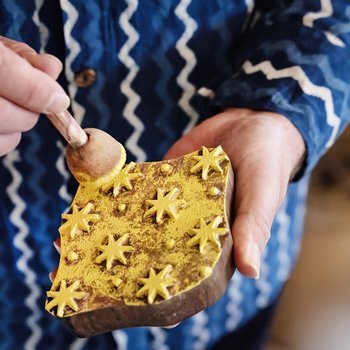 Photo of the artist holding a printing block about to print on to blue paper using yellow ink.