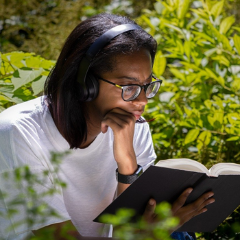 Person sat outside reading and wearing headphones