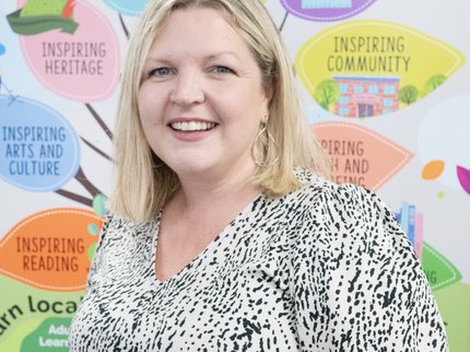 A woman in a black and white spotty dress and should length blonde hair smiles