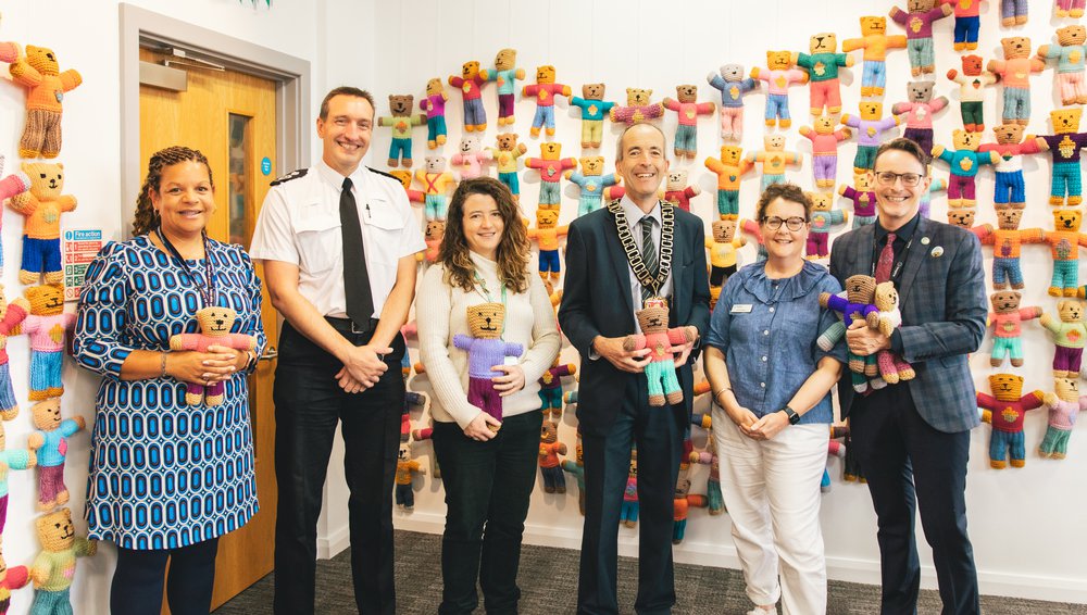 A group of people from partner organisations stand in a line holding a brave bear