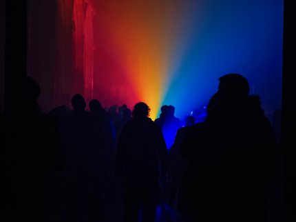 People standing in a dark church with lighting showing rainbow colours flooding up to the ceiling.