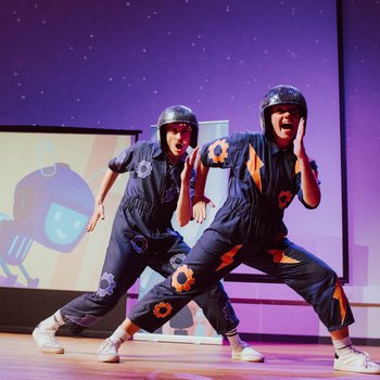 Two dancers with disco style helmets and purple jumpsuits strike a pose