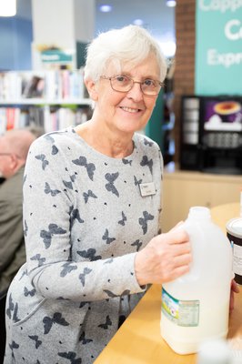 volunteer member of staff smiling holding a carton of milk