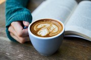 a cup of coffee with latte art next to an open book