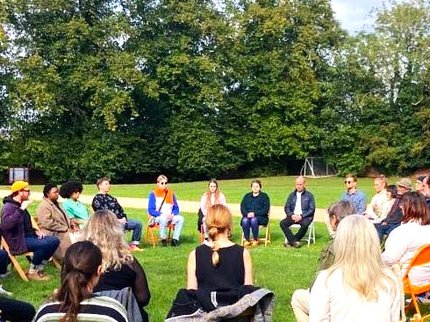 A group of people sitting in chairs outdoors in a circle with their eyes closed.