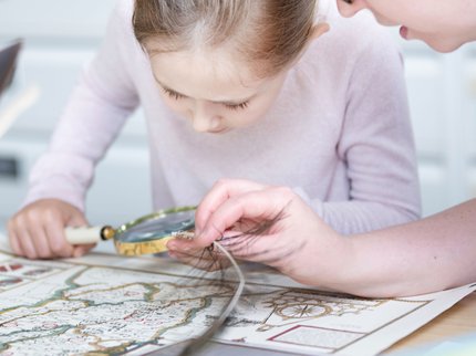 A girl holding a magnifying glass and looking at an historical map, assisted by a female archivist.