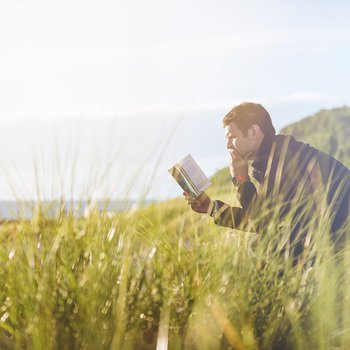 Man sat on a bench outside reading