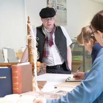 A group review historical documents while a man in costume speaks to them