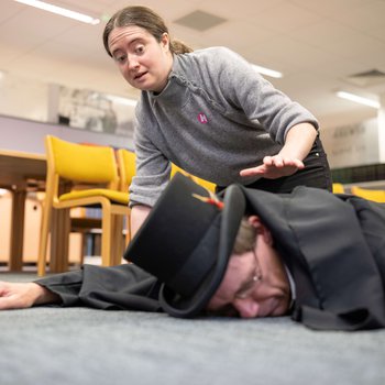 A person lies on the floor while another looks concerned