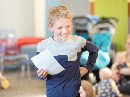 a young boy stood up smiling holding a slip of paper