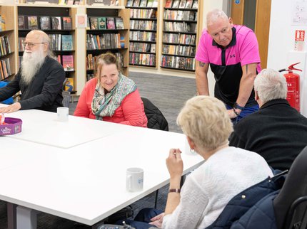 Group of people sat around a table drinking tea and coffee, at a library Places of Welcome group