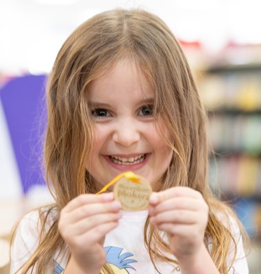 A smiling girl holds up her Summer Reading Challenge Medal